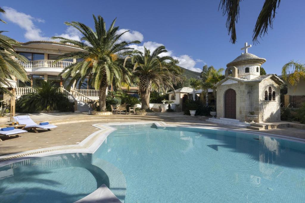 a large swimming pool with a church and palm trees at Villa Visanty with Private Pool & Access to Beach in Aigosthena