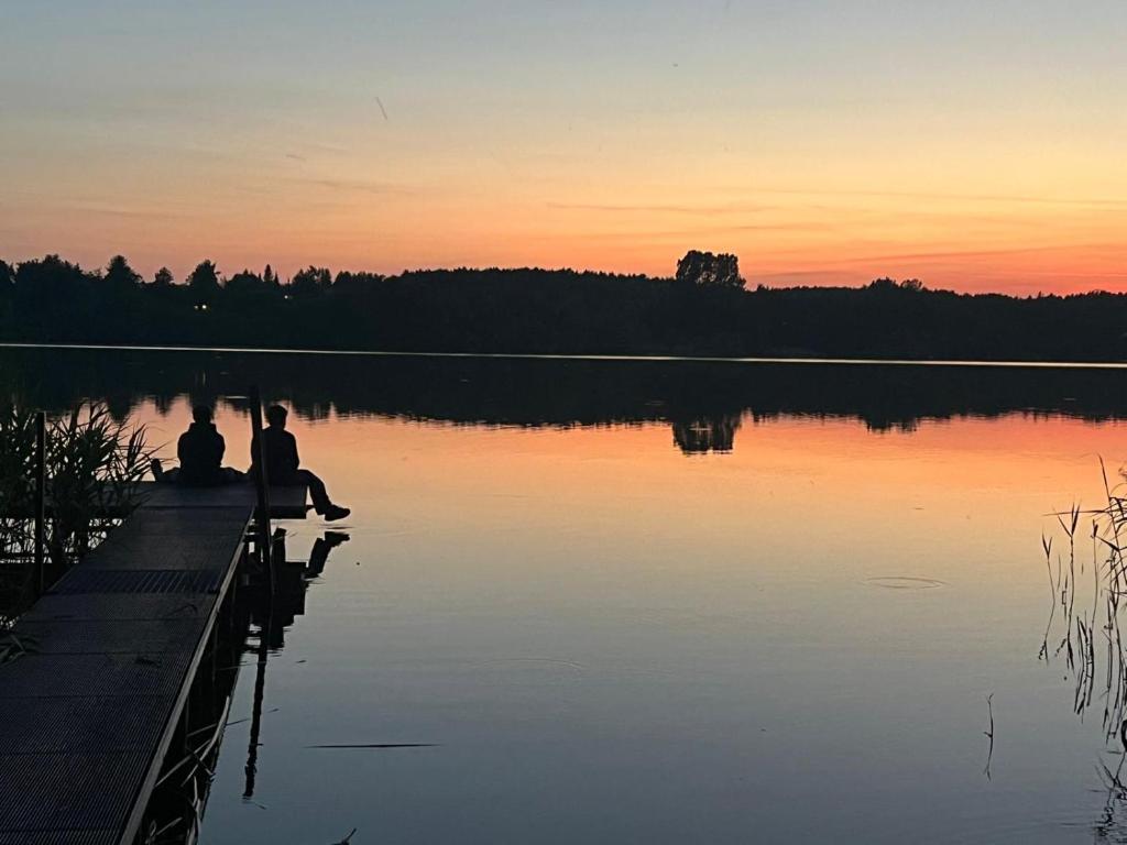 two people sitting on the dock of a lake at sunset at Dom Acapulco in Kromszewice