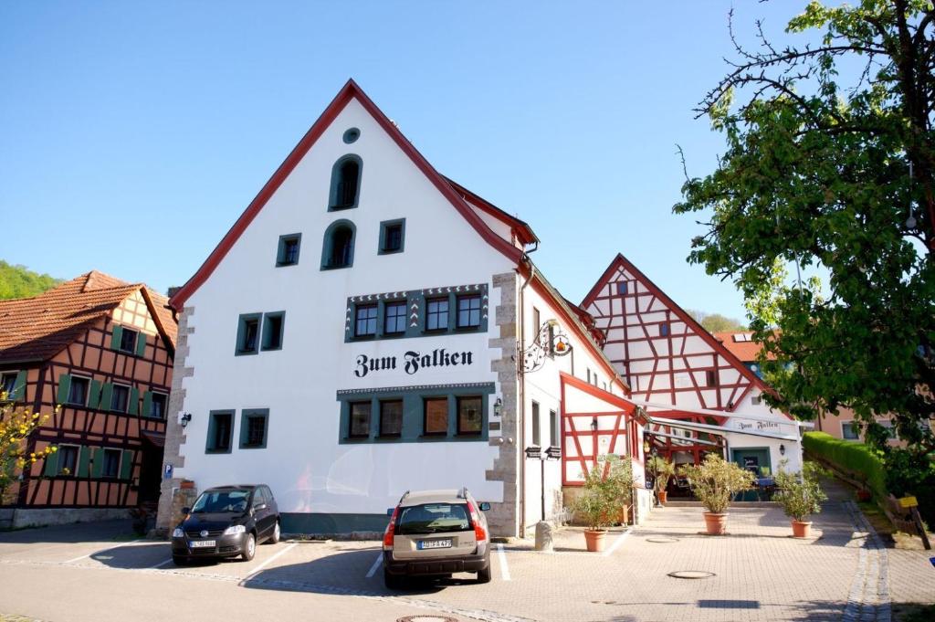 Un gran edificio blanco con coches aparcados en un estacionamiento. en Landhaus Zum Falken, en Tauberzell
