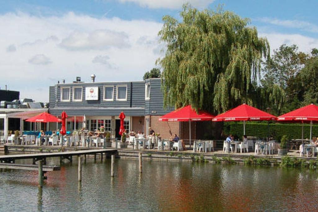 a restaurant with tables and red umbrellas next to the water at Weromerie Premium Hotel and Apartment in Wormer
