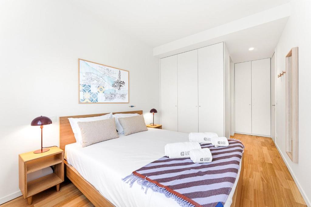 a white bedroom with a large bed with a striped blanket at GuestReady - Menéres Apartments in Matosinhos