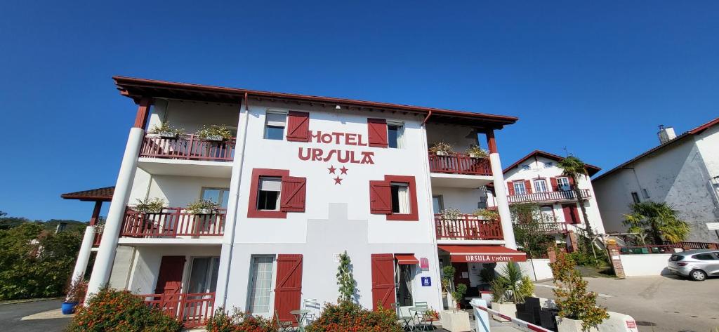 a white building with red doors and windows at Hôtel Ursula in Cambo-les-Bains