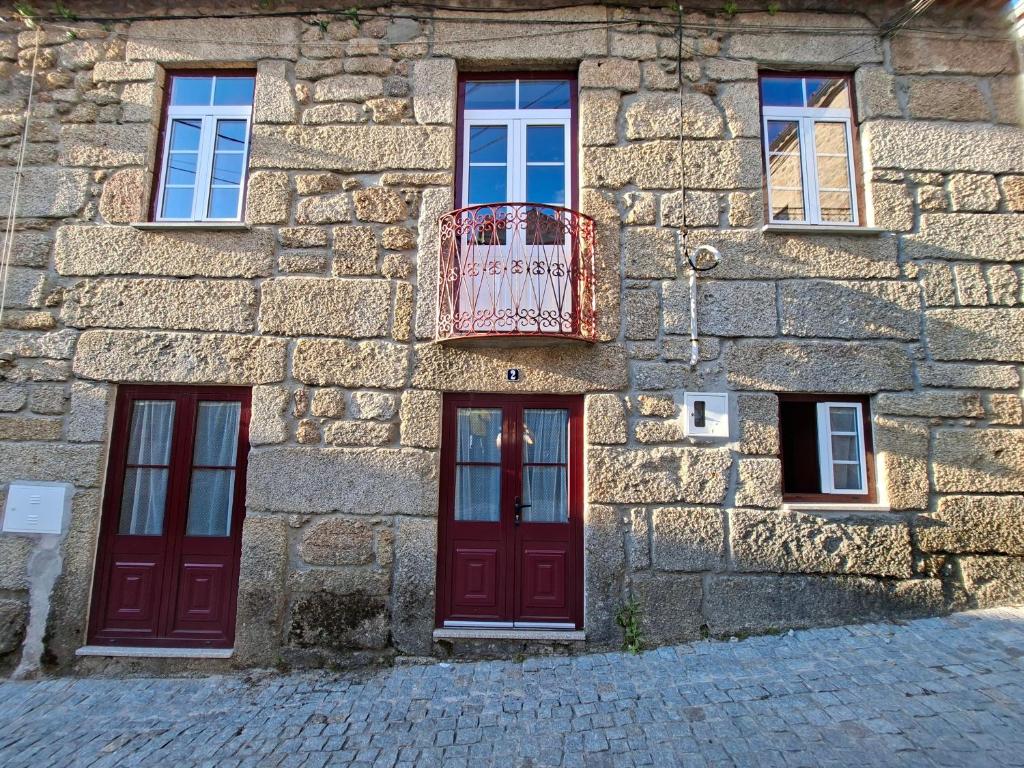 a stone building with red doors and a balcony at Big Alface - Casa de Cima in Trinta