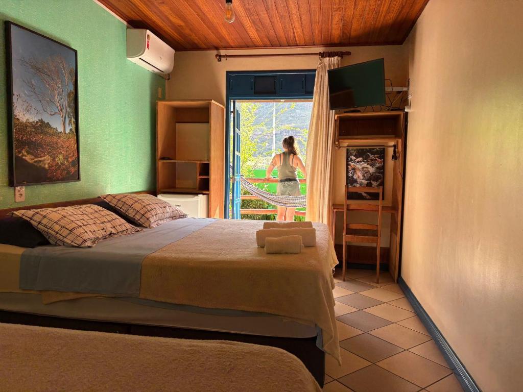 a bedroom with a bed and a woman looking out the window at Pousada Recanto da Chapada in Mucugê
