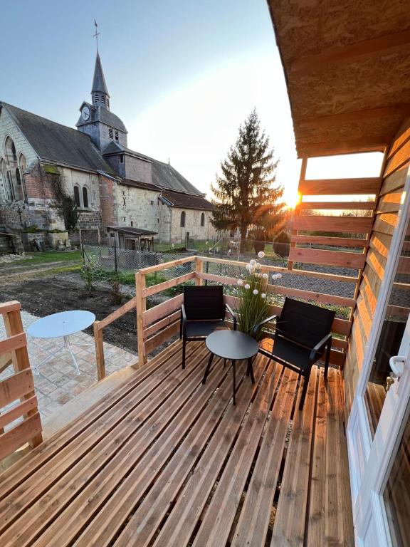 a wooden deck with chairs and a table and a church at La Roulotte des Gaillots in Moiremont