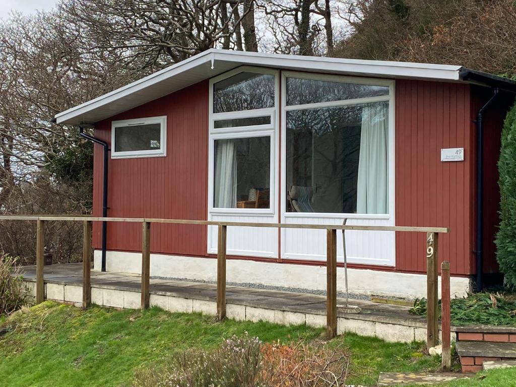 a red house with a white window and a fence at 49 Erw Porthor in Tywyn