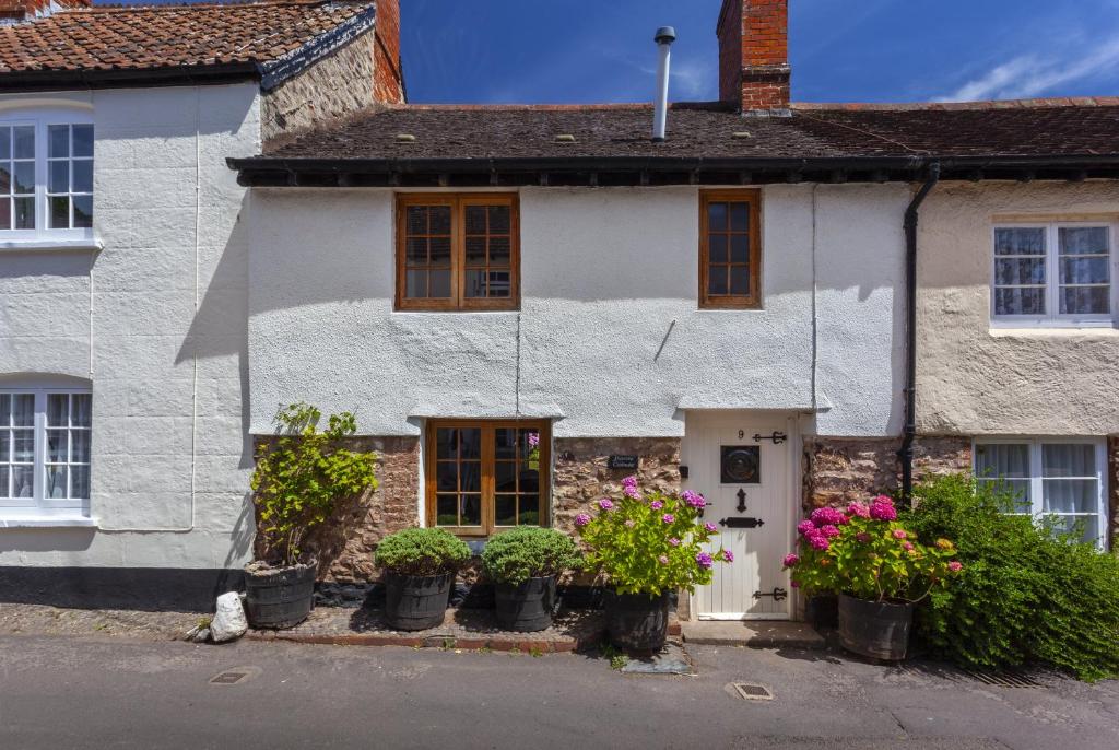 a white house with potted plants in front of it at Pebble Cottage Dunster in Dunster