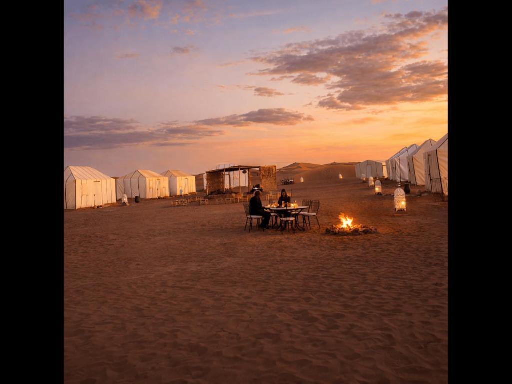 two people sitting at a table on a beach with tents at Chegaga Starlight Camp - Mhamid Desert Haven in Mhamid