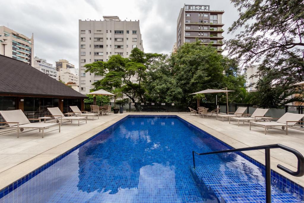 a swimming pool with chairs and umbrellas in a city at Victoria Place By HX in São Paulo