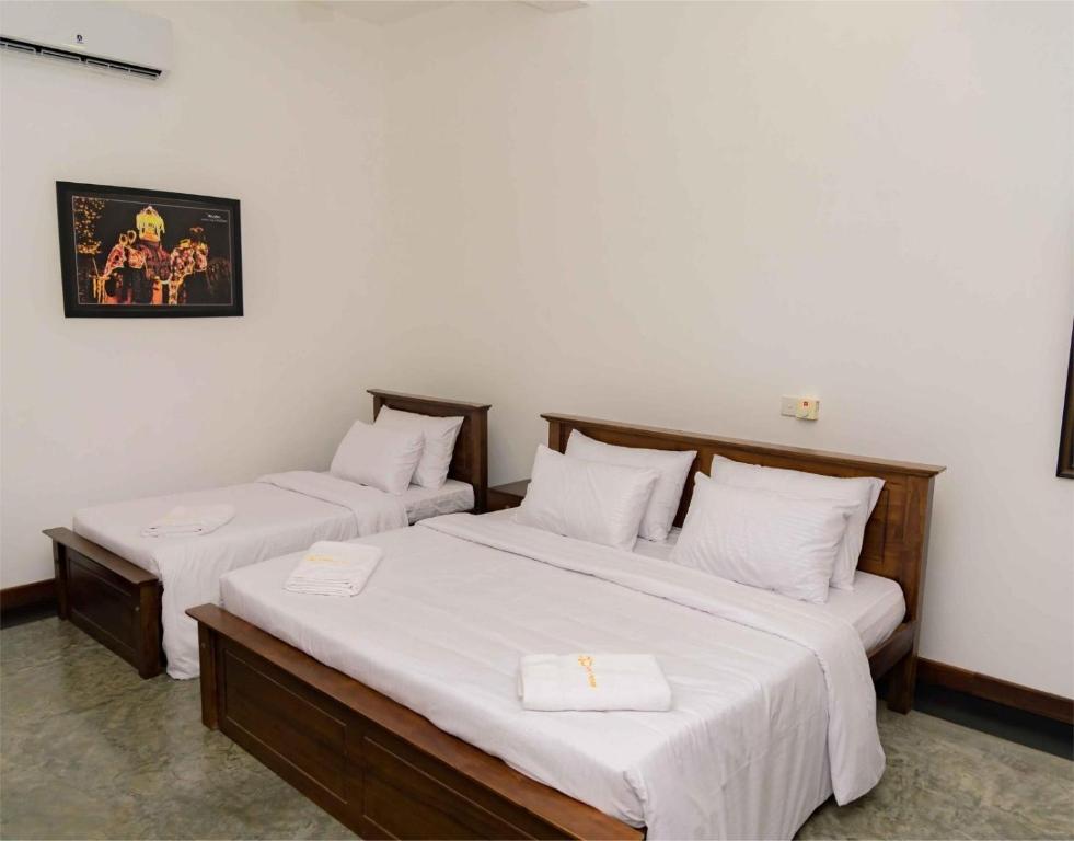 two beds in a room with white sheets at BTI Leisure Hotel in Kataragama