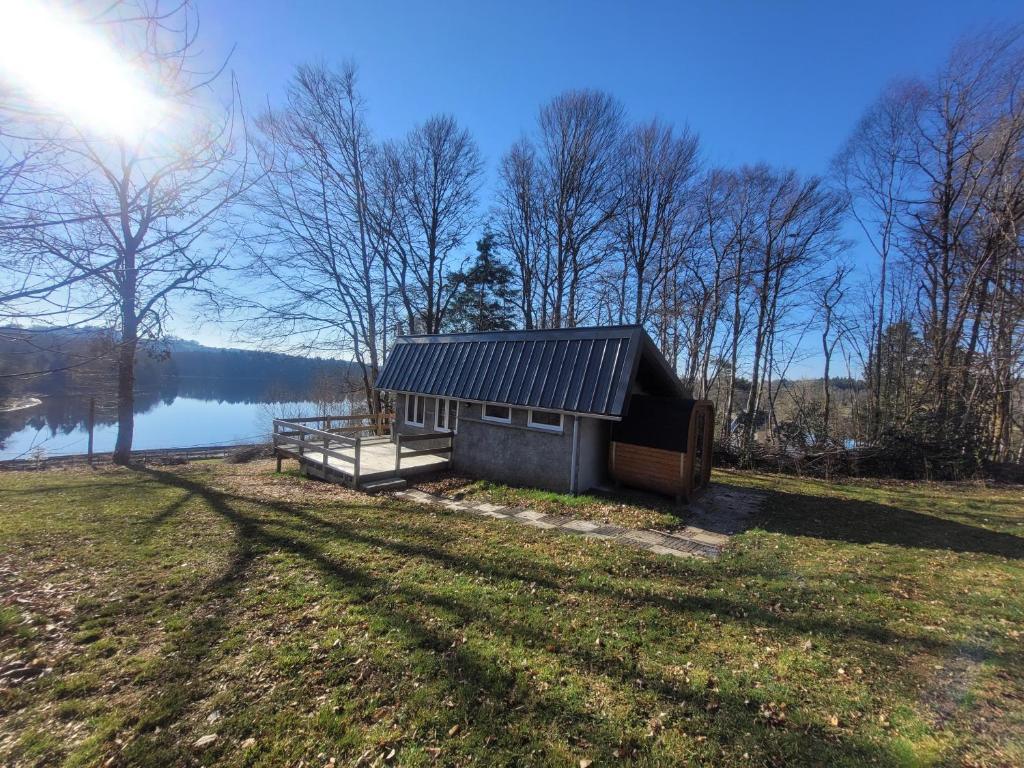 a small cabin in a field next to a lake at Petite maison vue sur Lac de la Triouzoune Neuvic in Neuvic