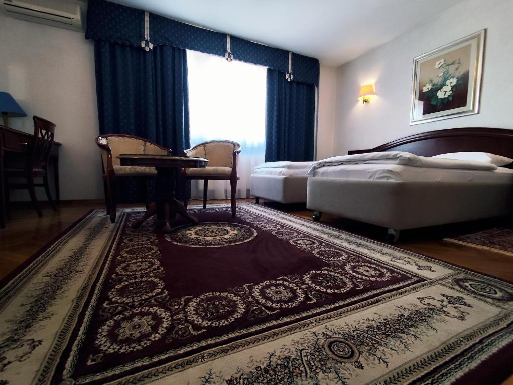 a bedroom with two beds and a table and a rug at Hotel Vila Ariston in Osijek