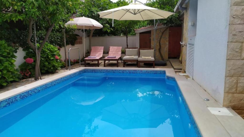 a swimming pool with chairs and an umbrella at Villa Katina Supetar with private pool, pool table, barbecue in Supetar