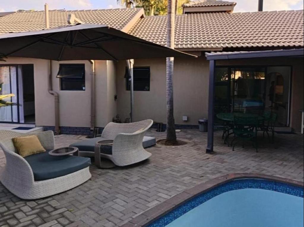 a patio with chairs and an umbrella next to a pool at Lady Daisy Boutique Guesthouse in Rustenburg