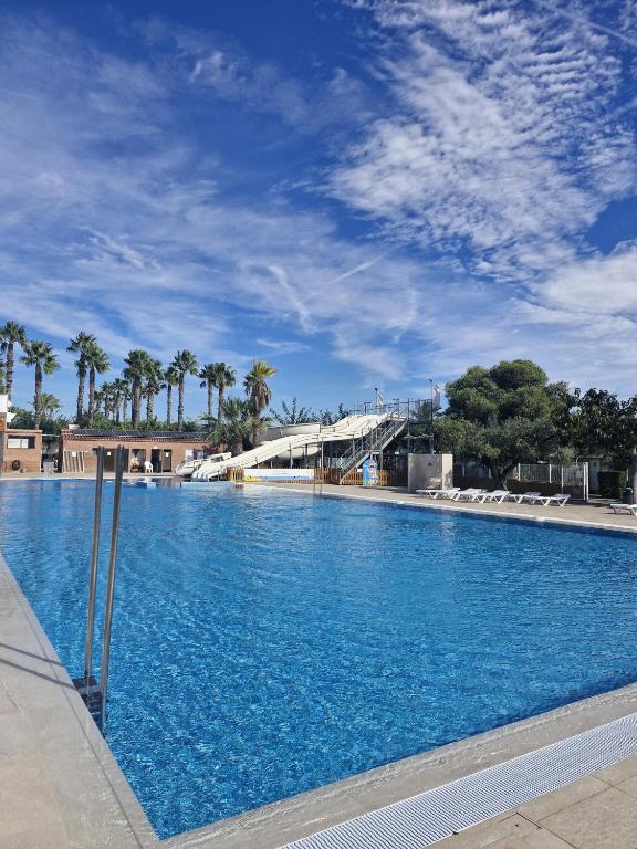 a large swimming pool with blue water and palm trees at Camping Platja Cambrils in Cambrils