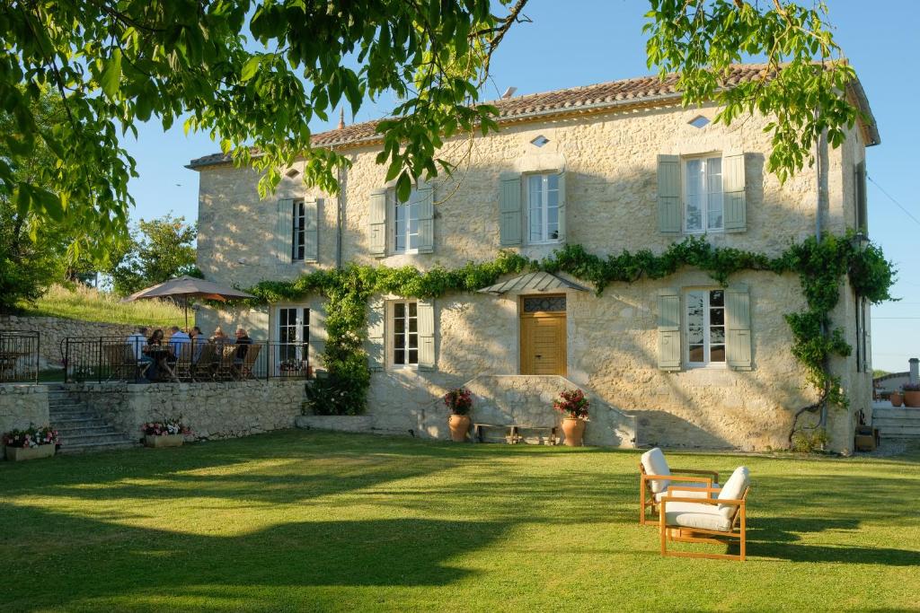 a large stone house with people sitting on a lawn at Plates Luxury Farm House Chambres d'hôtes et gîte in Saint-Mézard