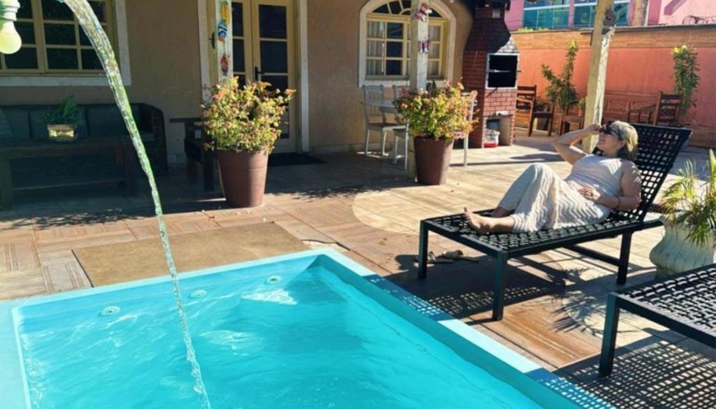 a woman sitting on a bench next to a swimming pool at Casa Espaço Pérola in Rio das Ostras