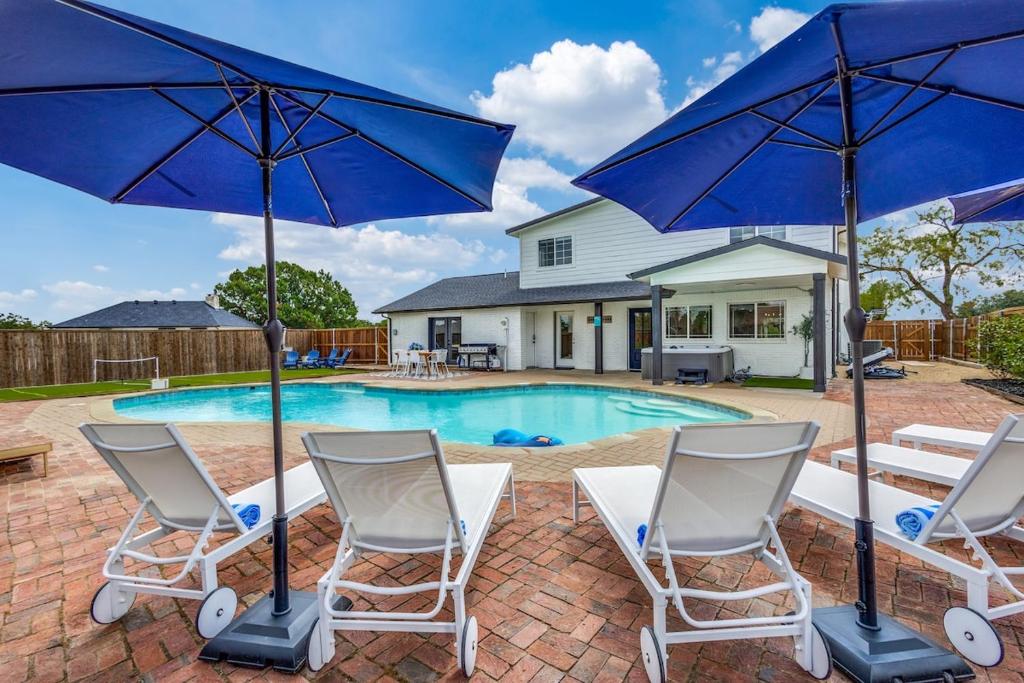 a pool with two chairs and two blue umbrellas at LWV Dallas Social - Lakewood Village in Little Elm