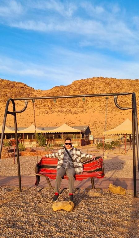 a man sitting on a bench in the desert at Rayyan Bedouin life camp in Wadi Rum