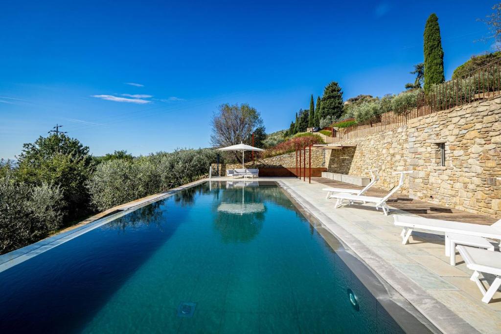 a swimming pool with two white chairs and a stone wall at YD exclusive design villa Agati in Castiglion Fiorentino