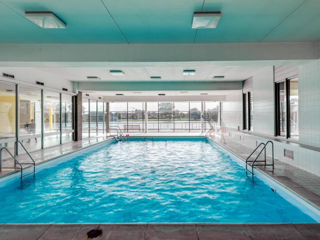 a large pool with blue water in a building at Casiola - Apartment with lake view & common indoor pool in Knokke-Heist