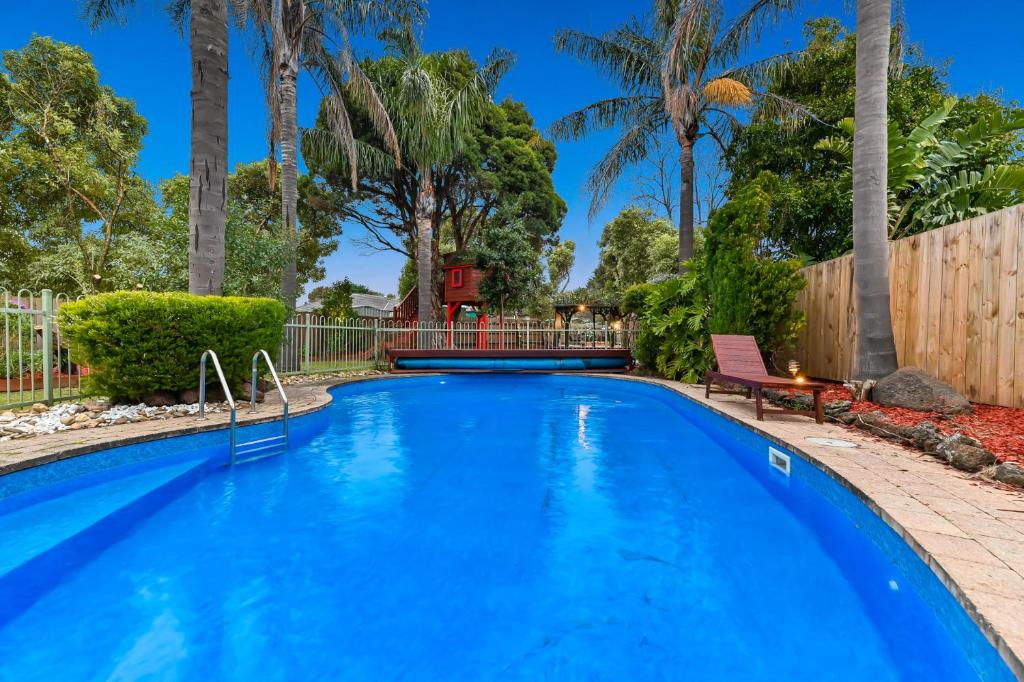 a large blue swimming pool in a yard with palm trees at Relax Refresh Rejuvenate Pool Cabin Garden Tree house Vintage charm in Berwick