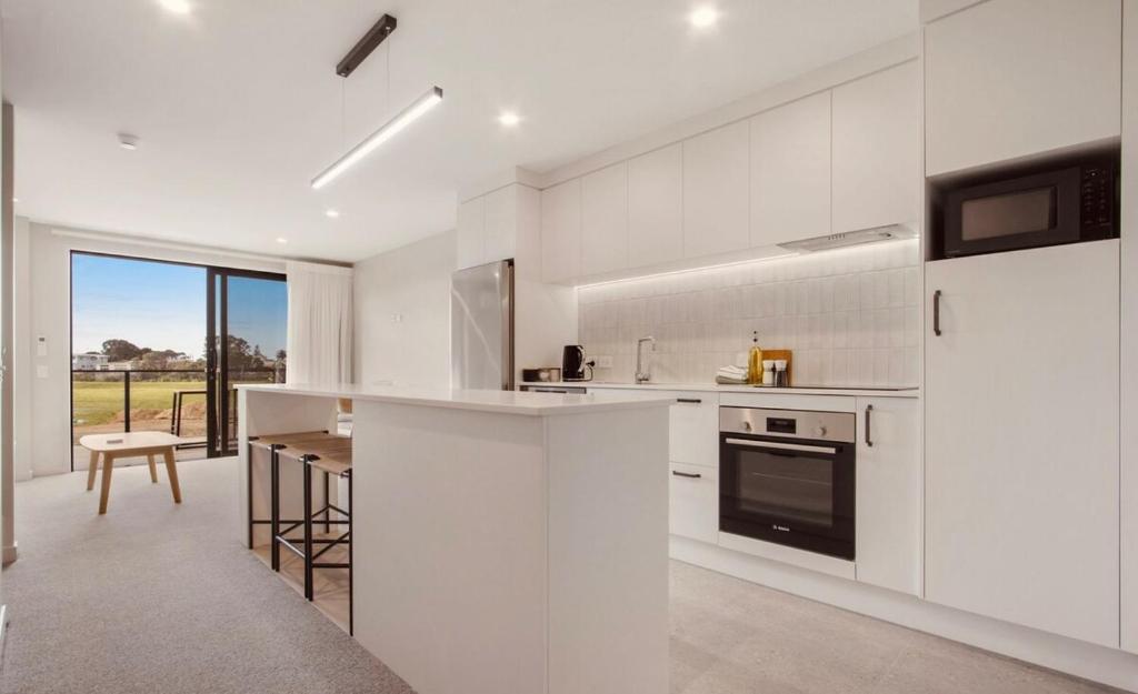 a white kitchen with a counter and a table at Waihi Beach Oasis - Apartment B1 in Waihi Beach