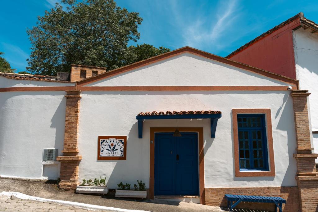 a small white building with a blue door at Clan.Destino Hostel in Ilhabela