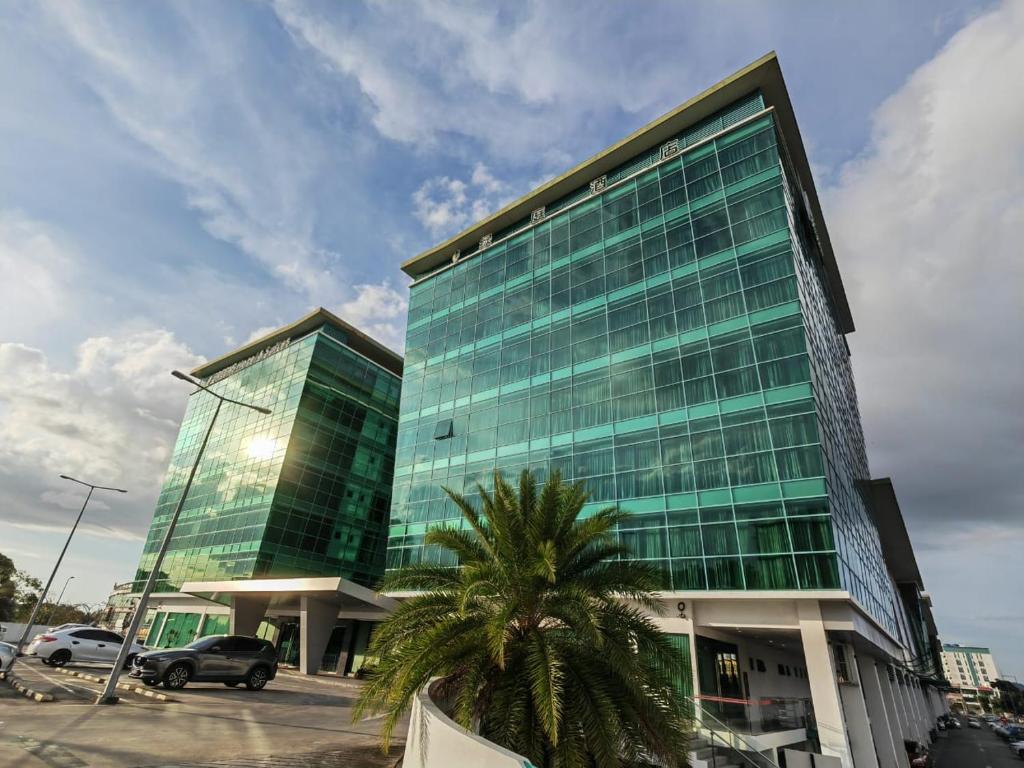 a tall glass building with a palm tree in front of it at Greens Hotel & Suites in Bintulu