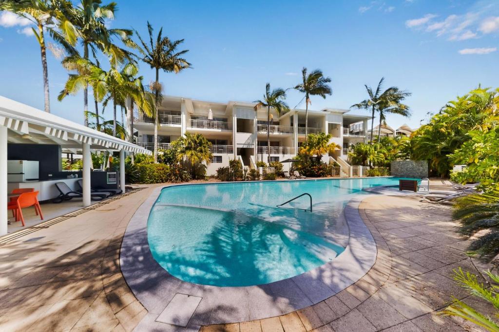 a swimming pool in front of a building with palm trees at Tidal Haven in Noosaville