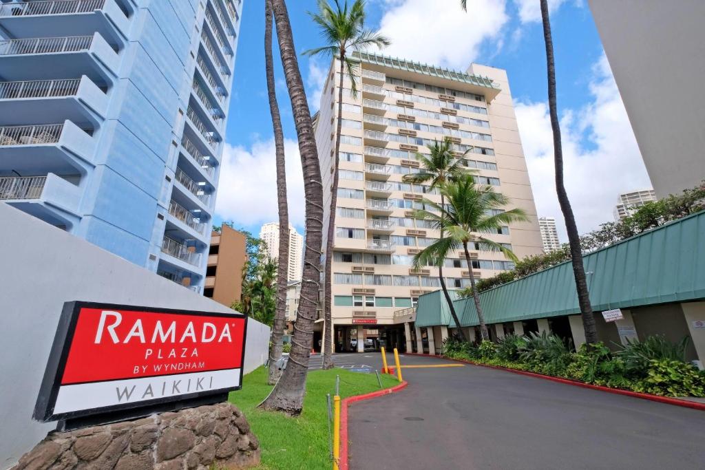 a sign in front of a building with palm trees at Ramada Plaza by Wyndham Waikiki in Honolulu