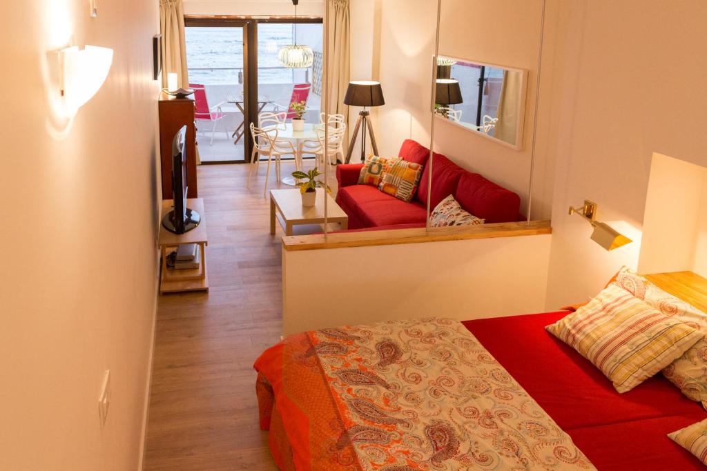 ラスパルマス・デ・グランカナリアにあるLiving Las Canteras Homes - BEACHFRONT OPEN TERRACEのベッドルーム1室(赤いベッド1台付)、リビングルームが備わります。