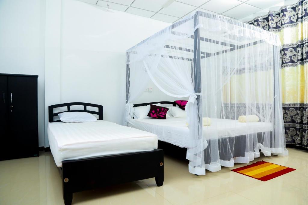two beds in a room with white walls and curtains at Anila Beach Inn in Tangalle