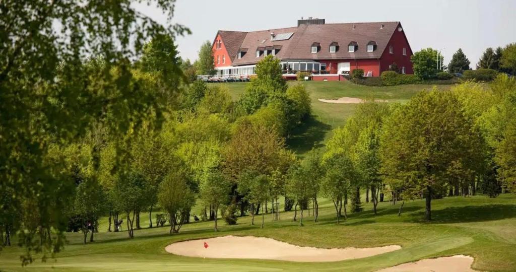 a view of a golf course with a red barn at Béni golf club Clervaux hôtel & Restaurant in Eselborn