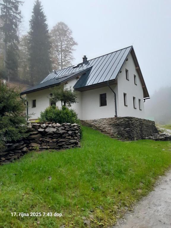 a white house with a slate roof and a stone wall at Chata AmBach in Liberk