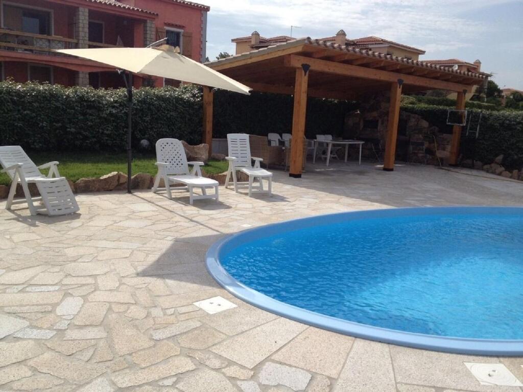 a pool with chairs and an umbrella next to a house at Apartment in a villa with a private pool in Cannigione