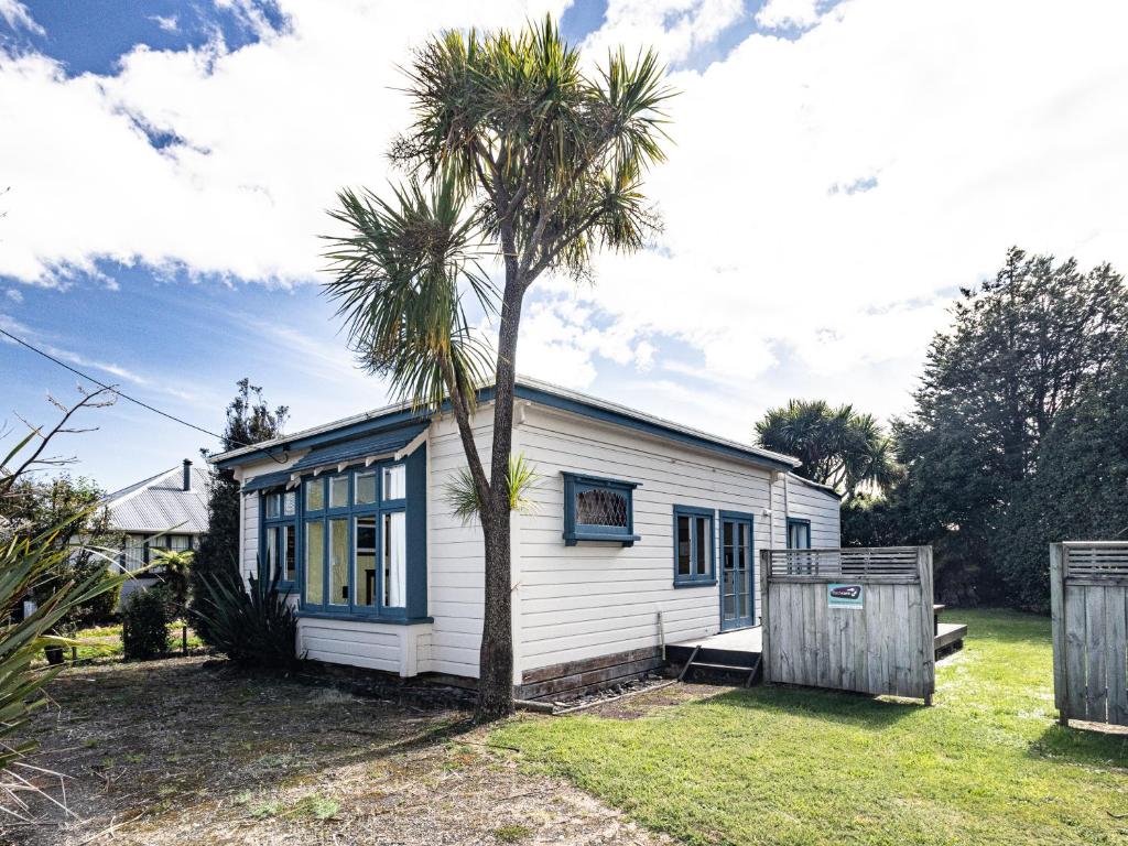 a small white house with a palm tree in the yard at Oroua Cottage - Rangataua Bach in Ohakune
