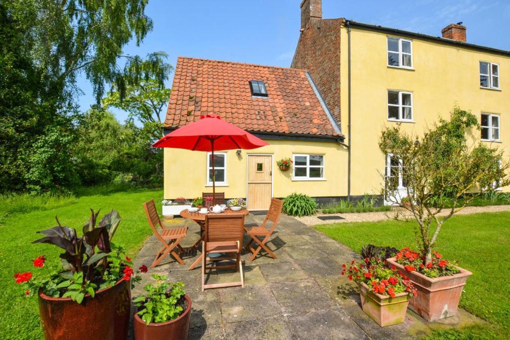 a table with a red umbrella in front of a house at 1 Bed in Bergh Apton oc-1387 in Thurton
