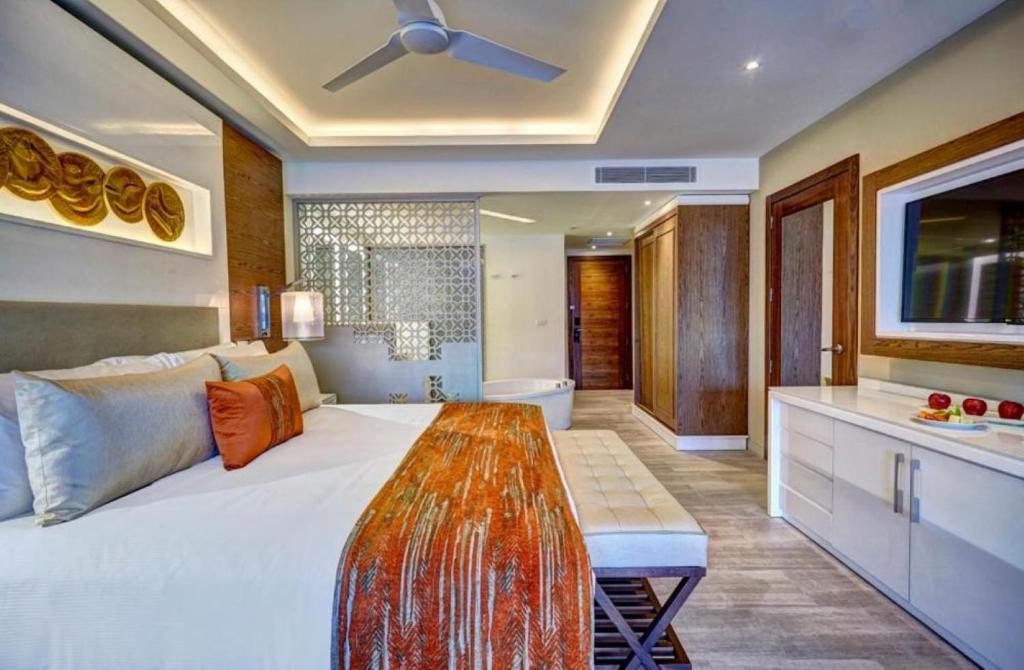 Suite bedroom with king bed, orange accents, living area, and bathroom visible.