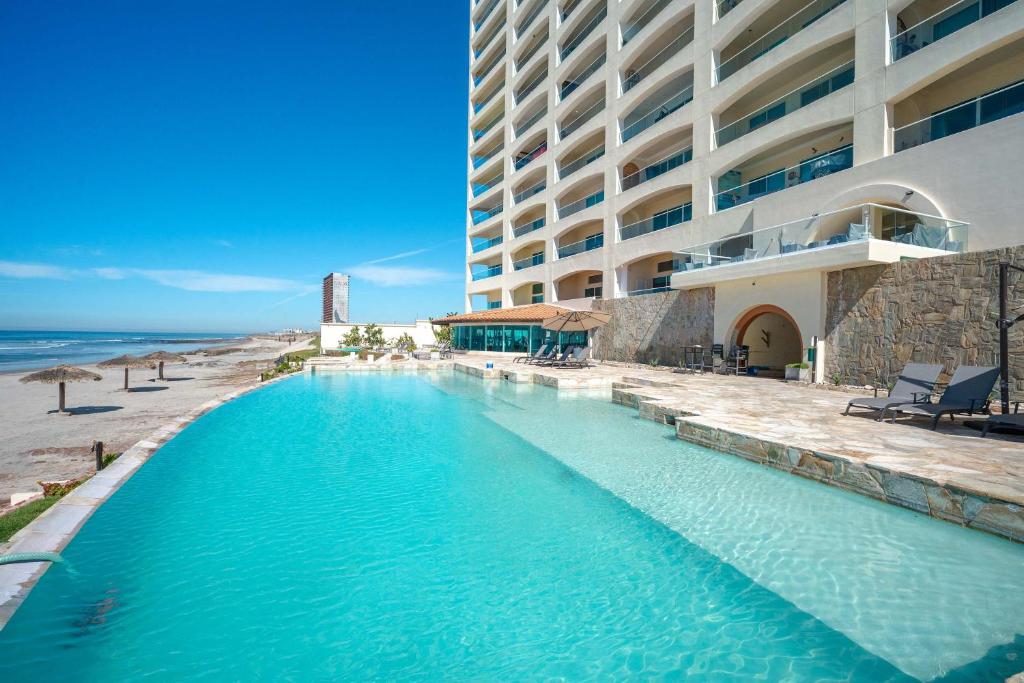 a swimming pool next to a hotel and the ocean at Mar y Sol 16th floor Condo in Rosarito