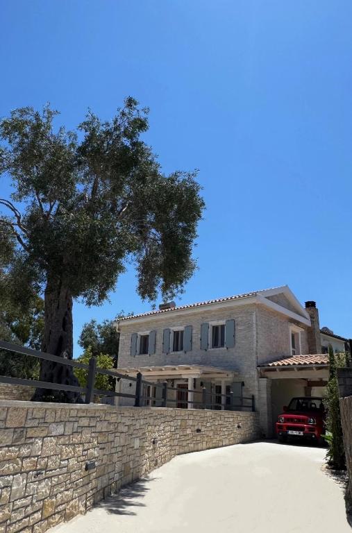 a house with a tree behind a stone wall at Geropalas Spacious Garden House in Vlachopoulátika