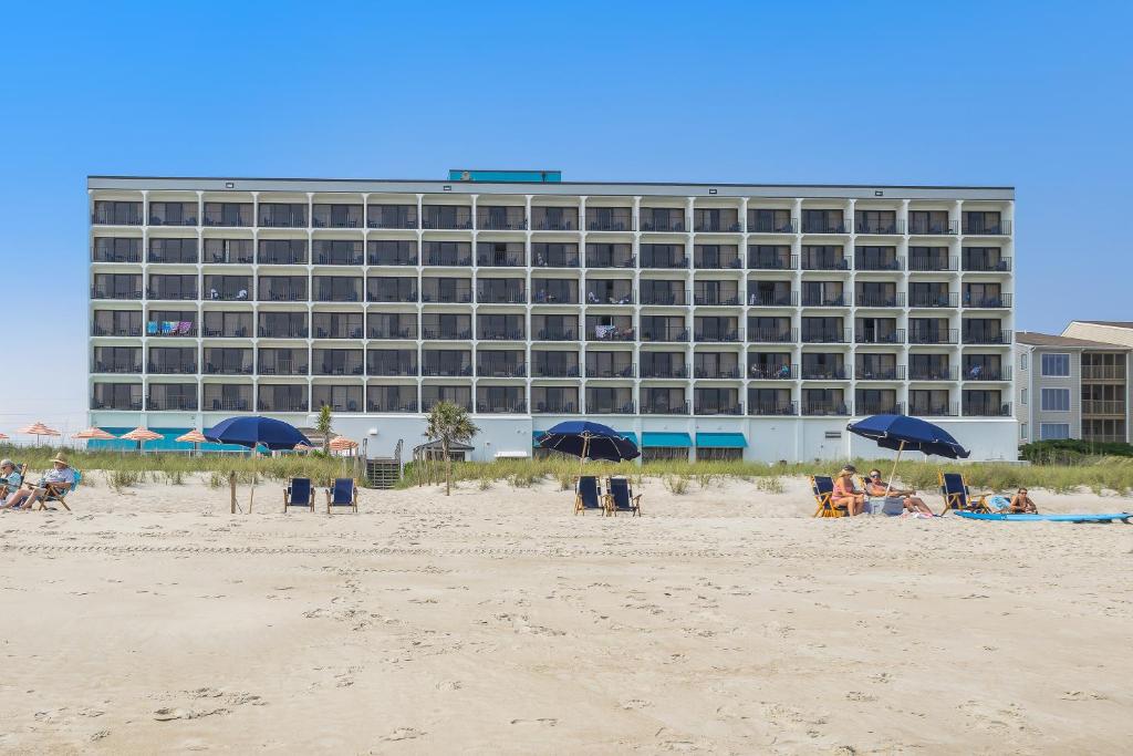 people sitting on the beach in front of a hotel at Crystal Coast Oceanfront Hotel in Atlantic Beach