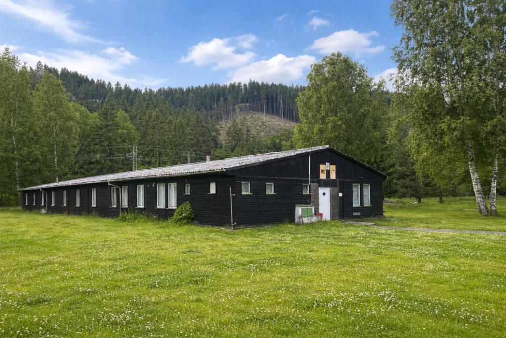 a black barn in a field of grass with trees at Wellness & Nature Hostel in Pirkenhammer