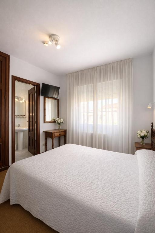 a bedroom with a large white bed and a window at Pensión Rey in Isla de Arosa