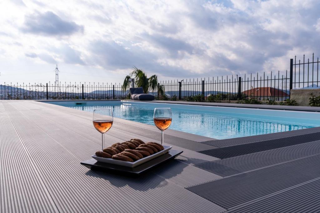 two wine glasses and a plate of food next to a swimming pool at Zafeiris House in Kalívia Thorikoú