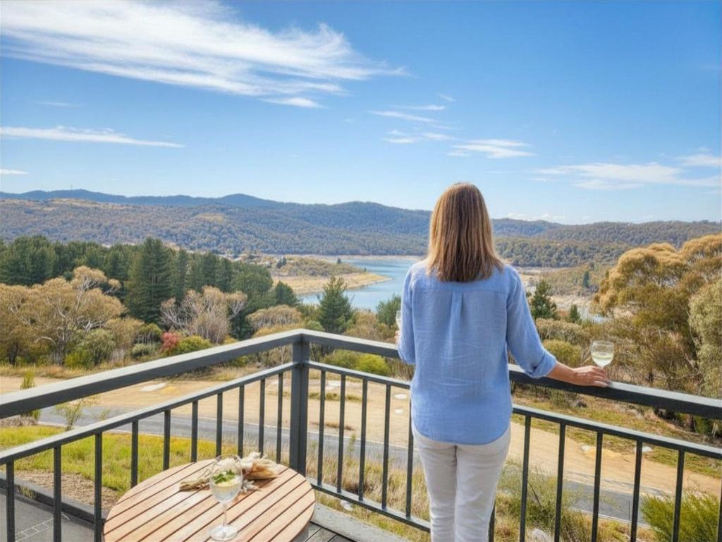 a woman standing on a balcony with a glass of wine at Lake Kami Retreat - Jindabyne in Jindabyne