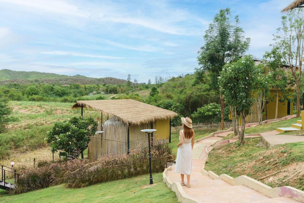 a woman standing on a walkway looking at a building at Mondara Villa and Glamping in Ban Bo Wi
