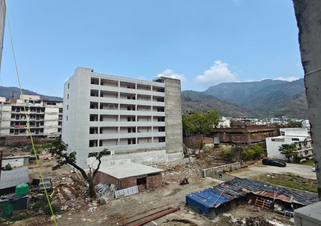 a tall white building in a city with mountains at VedaVibe Tapovan in Rishīkesh