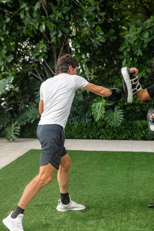 An outdoor grass area hosts a close-up fitness session beneath dense tropical planting.
