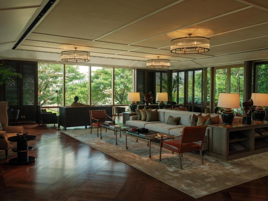 A broad lounge is arranged around sofas, armchairs and tall windows overlooking greenery.